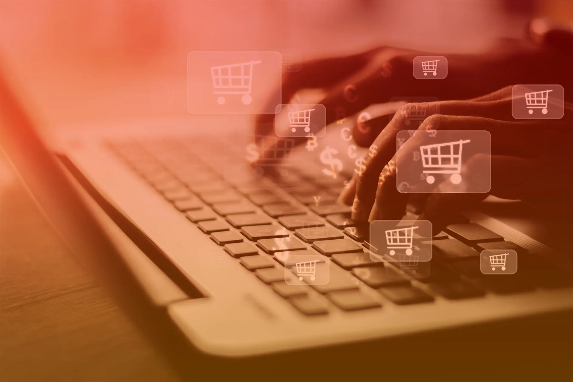 Dłonie na klawiaturze laptopa, nad którymi unoszą się ikony koszyków zakupowych